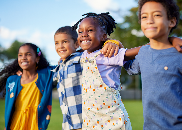 Four children happily posing outdoors with arms around each other.