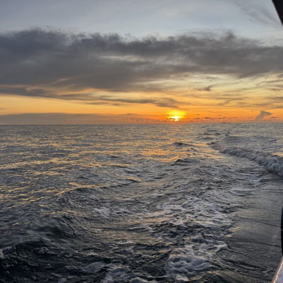 A serene sunset over the ocean with gentle waves and a partly cloudy sky.