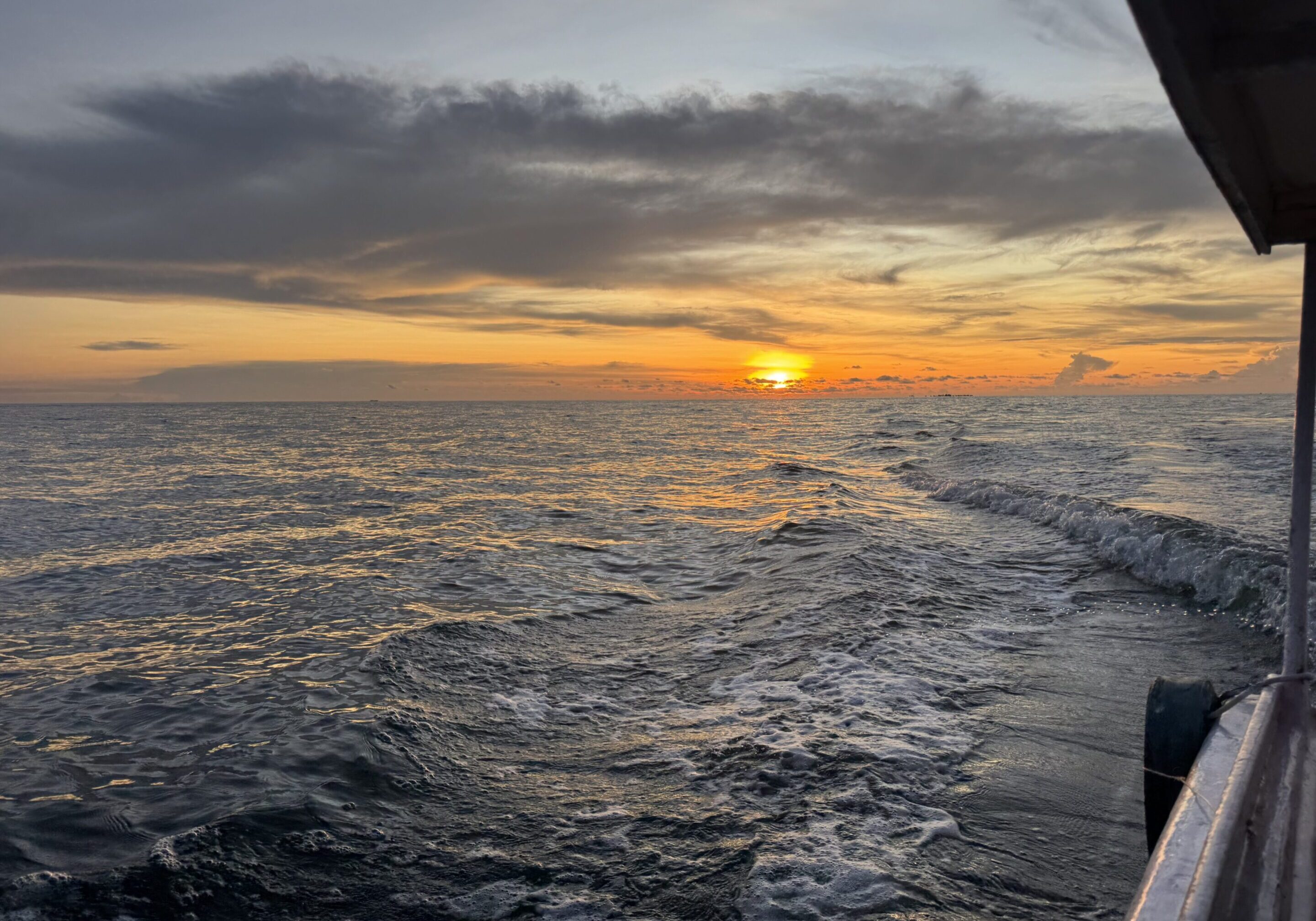 A serene sunset over the ocean with gentle waves and a partly cloudy sky.