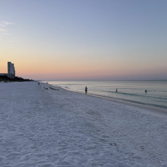 A peaceful beach scene at sunset with a lone figure near the water.